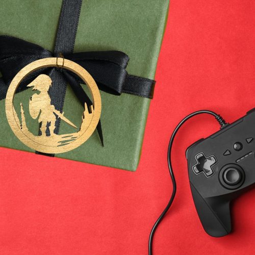 Legend of Zelda inspired wooden Christmas ornament decorating a wrapped gift beside a gaming controller.